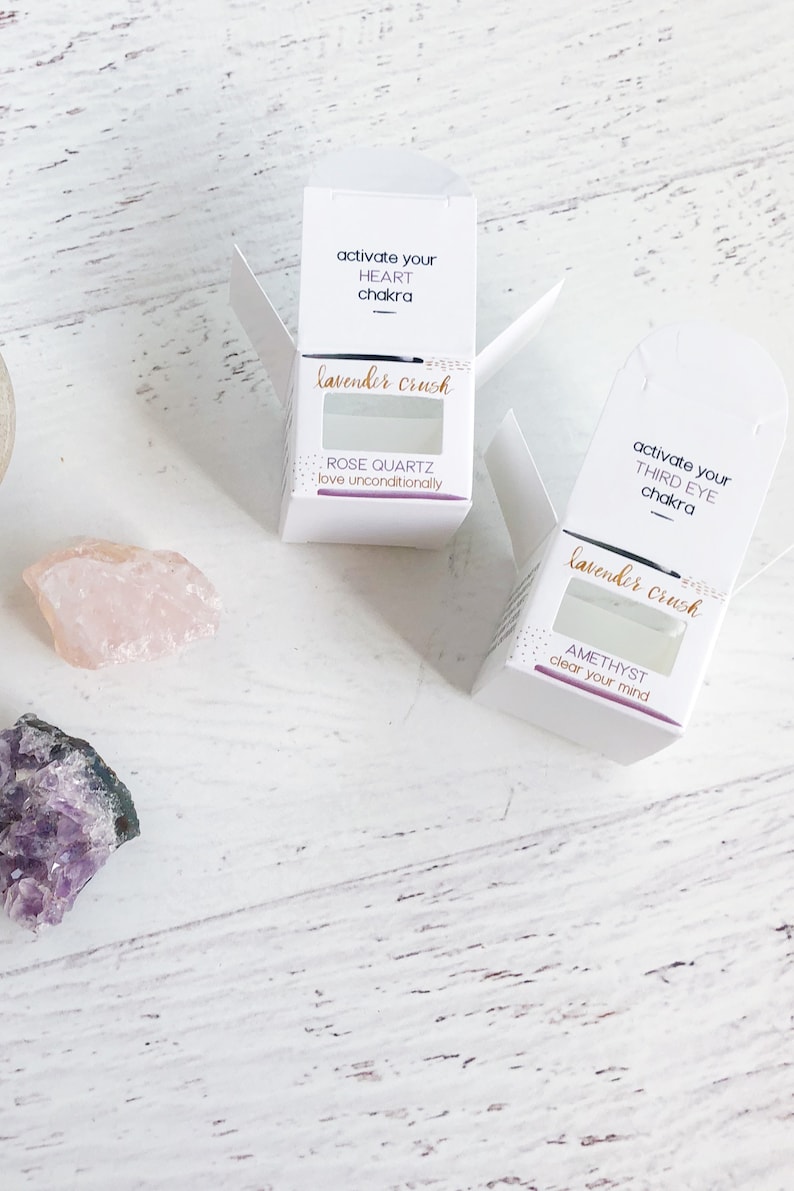 May include: Two white boxes with lavender crush written on them. The boxes contain crystals and are labeled with the chakra they are associated with. The top box is labeled "activate your heart chakra" and contains rose quartz. The bottom box is labeled "activate your third eye chakra" and contains amethyst.