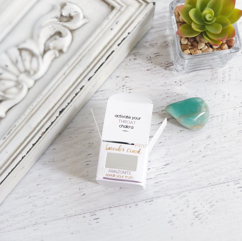 K&ouml;nnte beinhalten: Eine wei&szlig;e Box mit dem Text "activate your throat chakra" und "lavender crush" darauf. Die Box ist ge&ouml;ffnet und zeigt einen kleinen grauen Stein mit dem Text "AMAZONITE speak your truth" darauf.