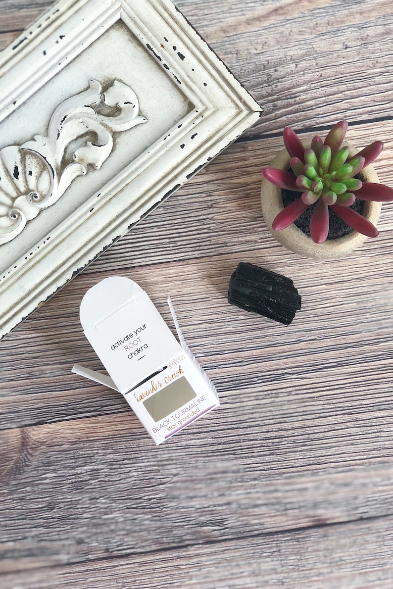 May include: A small white box with the text "activate your ROOT chakra" and "lavender crush" on it. The box contains a small piece of black tourmaline crystal. The text on the box also says "BLACK TOURMALINE stay grounded".