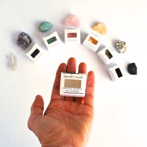 May include: A small white box with the text "lavender crush" and "CRYSTAL QUARTZ stay connected" on it. The box is being held in a person's hand.