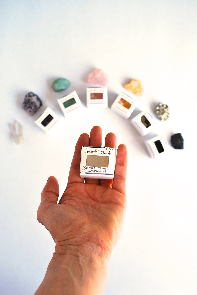 May include: A small white box with the text "lavender crush" and "CRYSTAL QUARTZ stay connected" on it. The box is being held in a person's hand.