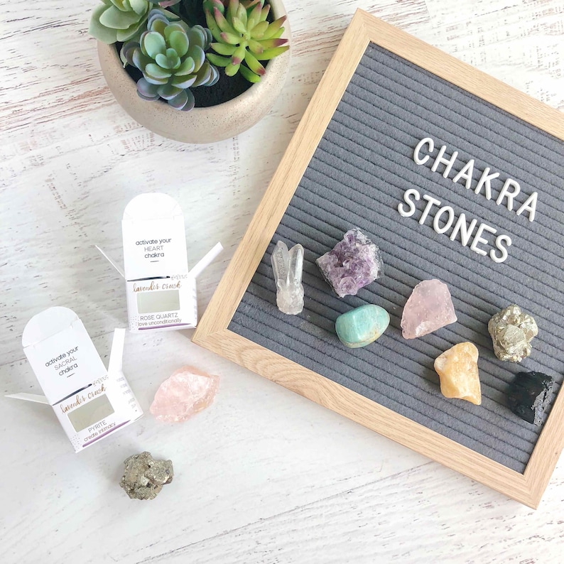 May include: A set of chakra stones with a letter board that reads "Chakra Stones". The stones are arranged in a row on the letter board. The stones are amethyst, rose quartz, turquoise, citrine, pyrite, and black obsidian. There are two small boxes with the text "activate your HEART chakra" and "activate your SACRAL chakra" on them.