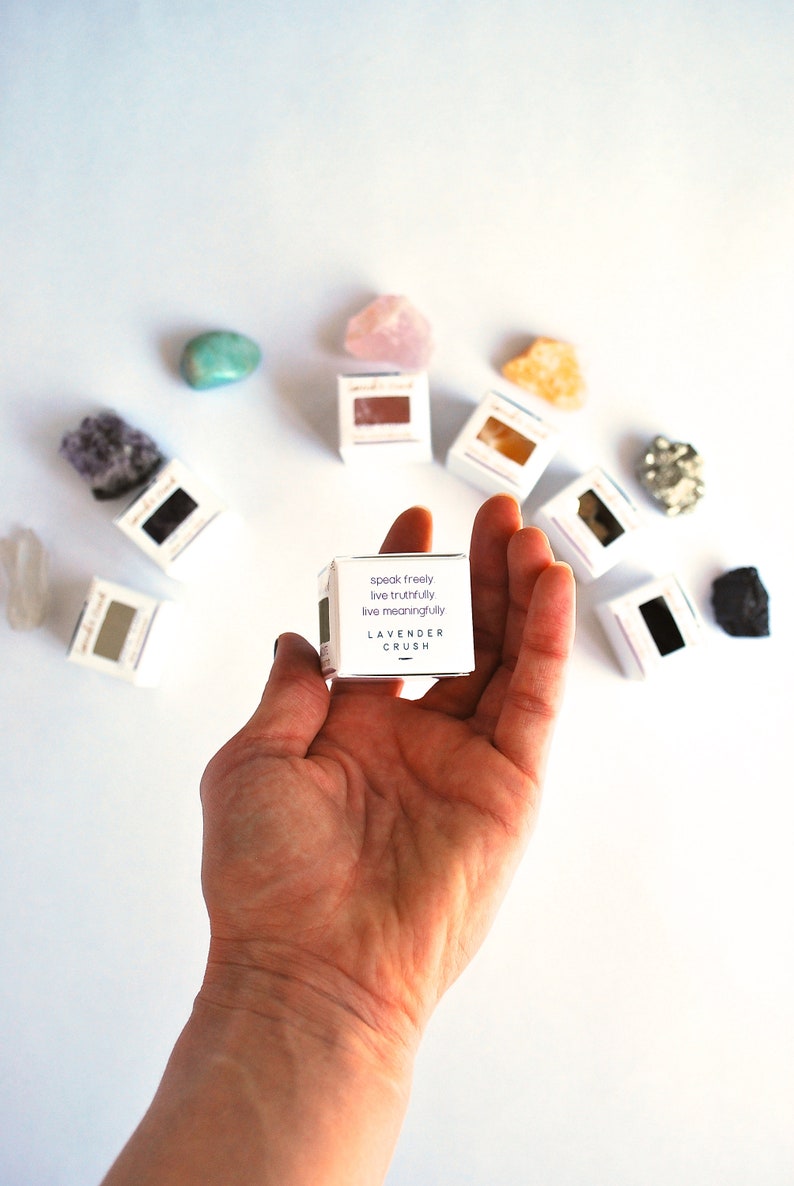 May include: A small white box with the text "speak freely, live truthfully, live meaningfully" and "LAVENDER CRUSH" printed on it. The box is being held in a hand against a white background.