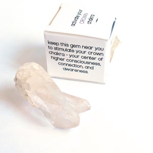 May include: A white box with the text "activate your CROWN chakra" and the text "keep this gem near you to stimulate your crown chakra - your center of higher consciousness, connection, and awareness." A clear quartz crystal is in the foreground.