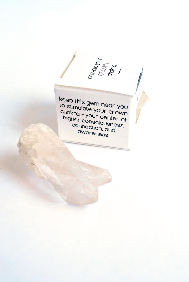 May include: A white box with the text "activate your CROWN chakra" and the text "keep this gem near you to stimulate your crown chakra - your center of higher consciousness, connection, and awareness." A clear quartz crystal is in the foreground.