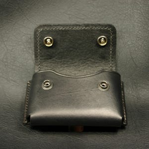 May include: A black leather wallet case with a flap closure and four brass rivets. The case is open and empty.