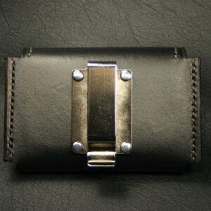May include: A black leather wallet with a silver metal clip. The wallet has a stitched edge and a smooth surface.