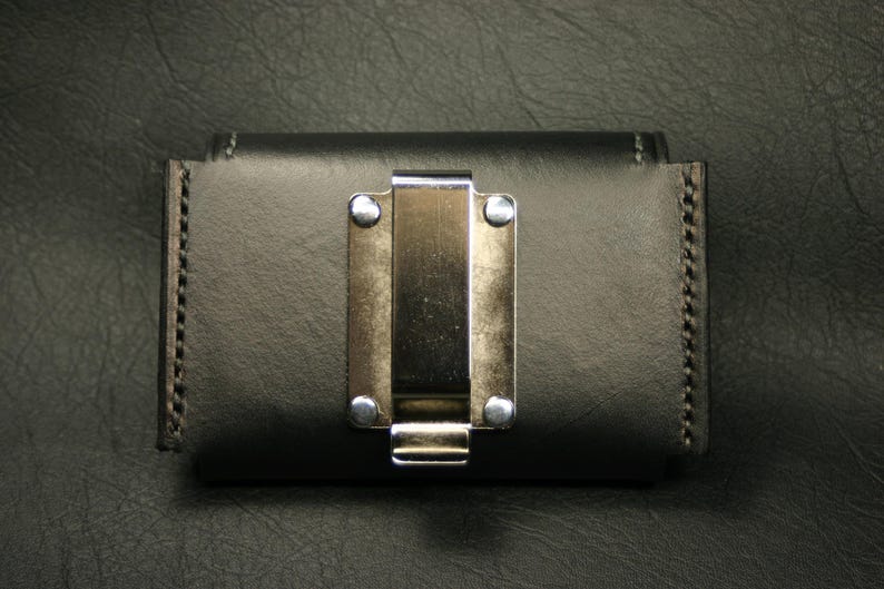May include: A black leather wallet with a silver metal clip. The wallet has a stitched edge and a smooth surface.