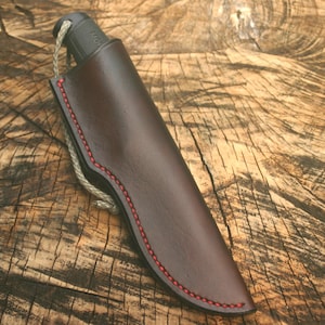 Peut inclure: Un fourreau de couteau en cuir marron avec des coutures rouges. Le fourreau a une boucle en haut pour une ceinture.