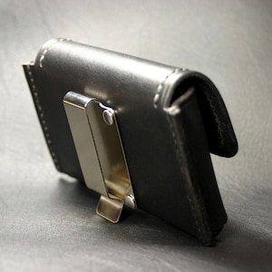 May include: A black leather wallet with a silver metal clip. The wallet has a stitched edge and a flap that closes with a snap.