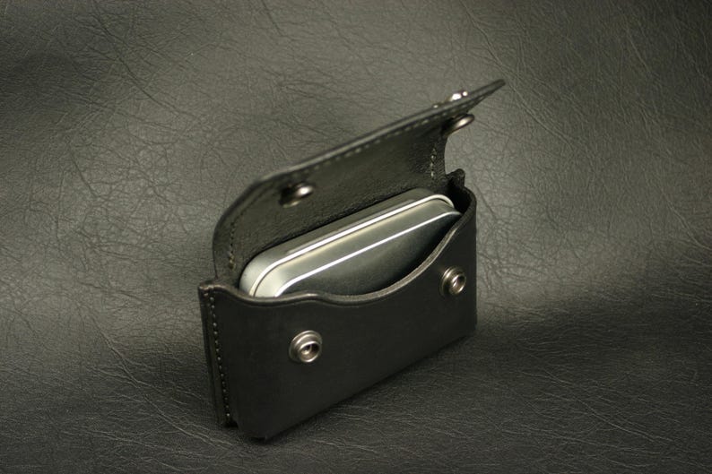 May include: A black leather case with a silver metal tin inside. The case has a flap that closes with a snap.