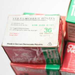 May include: A stack of three film canisters with red, white, and green labels. The top canister has the text "VEB FILMFABRIK WOLFEN" and "Made in German Democratic Republic". The middle canister has the text "OR WO CHROM" and "89 IT". The bottom canister has the text "OR WO CHROM" and "18".