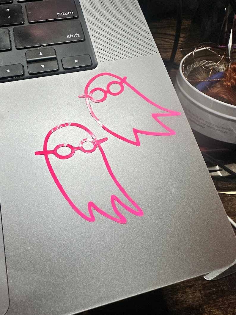 May include: Two pink ghost stickers with glasses on a silver laptop.