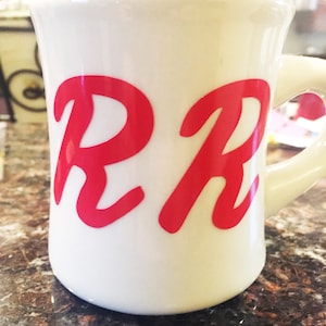May include: White ceramic mug with a red cursive "RR" design.