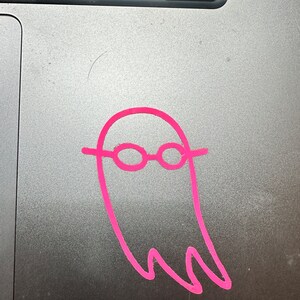May include: A pink ghost with glasses drawn on a silver laptop.