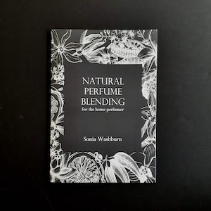 Peut inclure: Un livre intitulé "NATURAL PERFUME BLENDING for the home perfumer" de Sonia Washburn. La couverture noire est ornée d'illustrations florales blanches et d'un carré central contenant le titre et le nom de l'auteur.