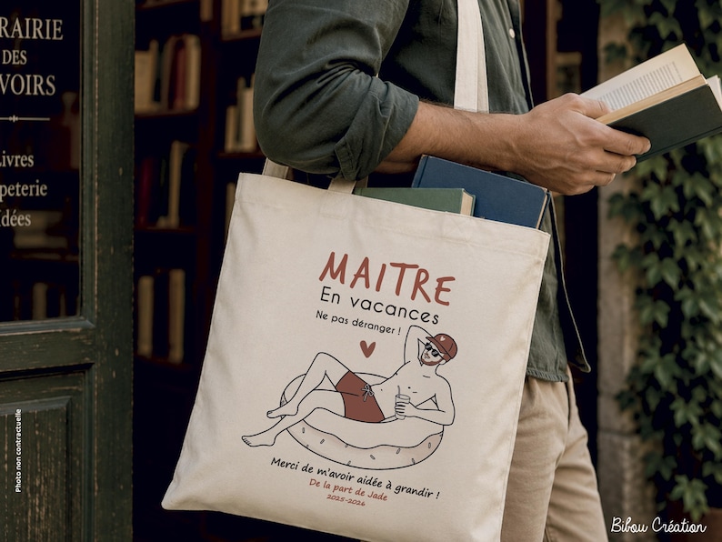 May include: A cream-colored canvas tote bag featuring a graphic illustration of a person relaxing on an inflatable pool ring. The text reads MAITRE En vacances Ne pas d&eacute;ranger ! Merci de m'avoir aid&eacute;e &agrave; grandir ! De la part de Jade 2023-2024.
