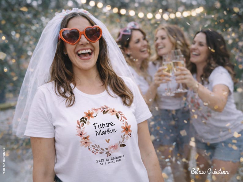 Op de afbeelding: Een vrouw met een hartvormige zonnebril en sluier lacht. Ze draagt een wit T-shirt met een bloemenkrans en de tekst "Future Mari&eacute;e". Andere vrouwen op de achtergrond houden champagneglazen vast. Confetti valt.