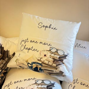 Peut inclure: Un coussin carr&eacute; blanc portant le pr&eacute;nom Sophie en haut, le texte just one more Chapter, et une illustration imprim&eacute;e d'une pile de livres, d'une tasse &agrave; th&eacute; bleue, d'une paire de lunettes et de petites fleurs avec des papillons.
