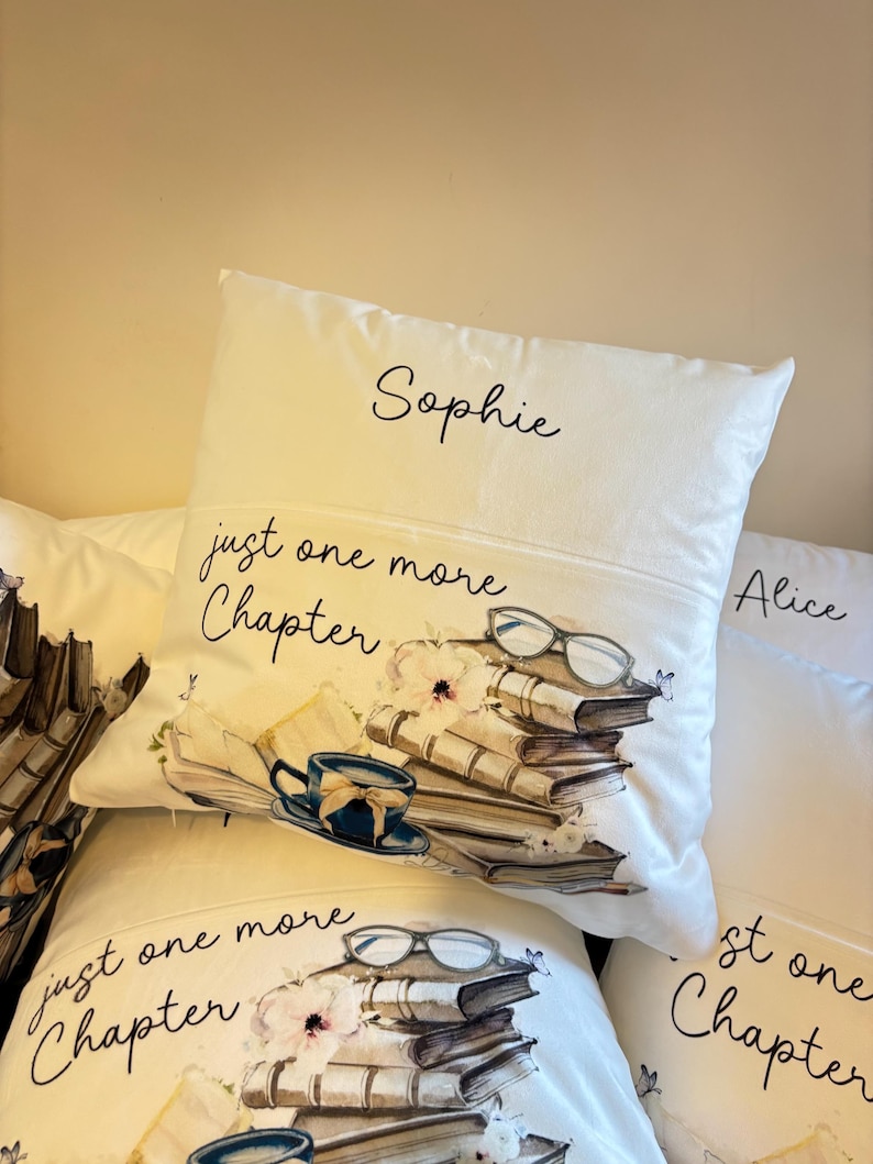 Peut inclure: Un coussin carr&eacute; blanc portant le pr&eacute;nom Sophie en haut, le texte just one more Chapter, et une illustration imprim&eacute;e d'une pile de livres, d'une tasse &agrave; th&eacute; bleue, d'une paire de lunettes et de petites fleurs avec des papillons.