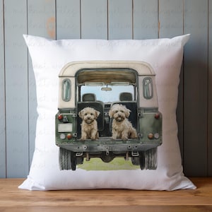 Puede incluir: Almohada blanca con un Land Rover verde y blanco con dos perros pequeños de color marrón claro sentados en la parte trasera. Los perros miran a la cámara.