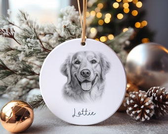 May include: A white ceramic Christmas ornament with a black and white pencil drawing of a golden retriever dog. The dog is smiling and the ornament has the name "Lottie" written on it.