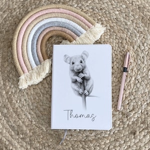 May include: A white notebook with a black and white illustration of a mouse on the front. The name "Thomas" is printed in black below the illustration.