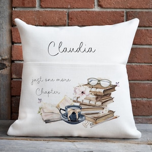 Peut inclure: Un coussin carr&eacute; blanc portant le pr&eacute;nom Claudia en &eacute;criture noire. En dessous, le texte just one more Chapter accompagne une illustration imprim&eacute;e d'une pile de livres, d'une tasse &agrave; th&eacute; bleu fonc&eacute;, de lunettes et de petits papillons.