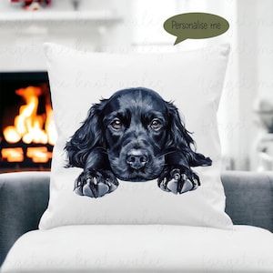 Puede incluir: Una almohada blanca con una ilustración de un perro Cocker Spaniel negro. El perro mira a la cámara con sus patas apoyadas en el borde de la almohada. El texto "Personalízame" está en un bocadillo de diálogo sobre el perro.