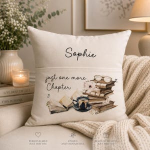 May include: A cream-colored square throw pillow featuring the name Sophie printed in black script at the top. Below, the text just one more Chapter appears alongside a printed illustration of a stack of books, eyeglasses, and a teacup.