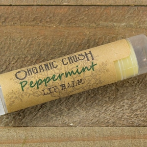 May include: A brown tube of Organic Crush Peppermint Lip Balm with a clear plastic cap. The label features a green leafy design and the text "Organic Crush Peppermint Lip Balm".