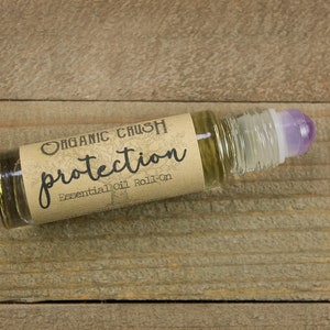 May include: A small glass bottle with a brown label that reads "ORGANIC CRUSH protection Essential Oil Roll-on". The bottle has a purple roller ball.