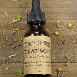 K&ouml;nnte beinhalten: Eine braune Glasflasche mit einer schwarzen Tropfflasche und einem Etikett mit der Aufschrift "ORGANIC CRUSH Forever Young Anti-Aging Facial Serum Revitalizing blend of oils for mature skin (1 OZ.)"