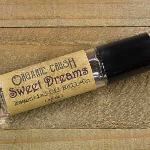 May include: A brown glass roll-on bottle with a black cap. The label reads "Organic Crush Sweet Dreams Essential Oil Roll-On (1/3 oz)".