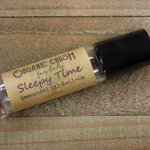 May include: A brown glass roll-on bottle with a black cap. The label reads "Organic Crush for baby Sleepy Time Essential Oil Roll-On".