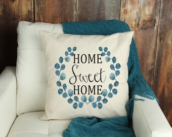 May include: A white throw pillow with a blue watercolor wreath and the text "Home Sweet Home" in black.