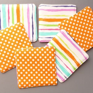 May include: A set of five square fabric coasters featuring two distinct patterns. Three coasters display a white background with orange polka dots, while two coasters feature a white background with multicolored vertical or horizontal stripes.