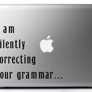 Op de afbeelding: Een zilveren laptop met een sticker waarop staat: "Ik corrigeer je grammatica stilletjes..."