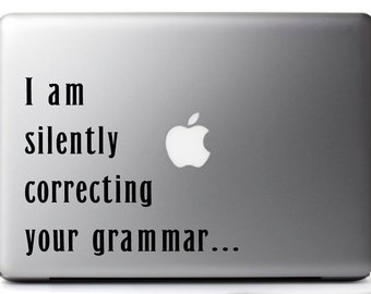 May include: A silver laptop with a sticker that says "I am silently correcting your grammar..."
