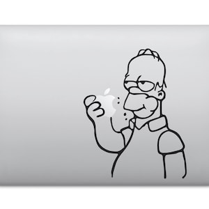 Könnte beinhalten: Schwarz-weißer Aufkleber mit einer Comicfigur mit gelbem Gesicht, die einen Apfel isst. Die Figur trägt ein blaues Hemd. Der Aufkleber befindet sich auf einem silbernen Laptop.