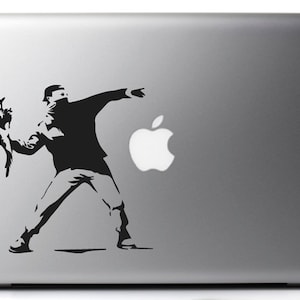 Può includere: Un adesivo in bianco e nero di una persona che lancia un fiore, con una maschera nera, su un laptop argentato con un logo Apple bianco.
