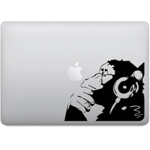 Könnte beinhalten: Schwarz-weiße Silhouette eines Affen mit Kopfhörern, der nachdenkt. Der Affe befindet sich auf einem silbernen Laptop mit einem Apple-Logo.