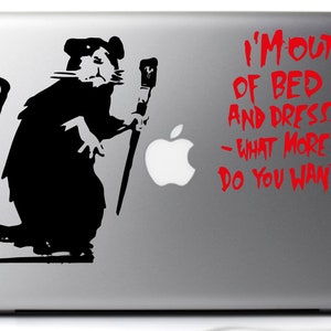 Può includere: Un laptop argentato con una silhouette in bianco e nero di un ratto che tiene un pennello e una grafica rossa che dice "I'm out of bed and dressed - what more do you want?"