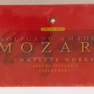 Puede incluir: Un conjunto de cajas rojas de las obras completas de Wolfgang Amadeus Mozart. El conjunto de cajas incluye 170 CD y presenta un retrato de Mozart en la parte delantera. El texto "Mozart 250 años" también es visible en la caja.
