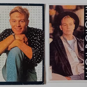 May include: Two trading cards featuring a young man with short brown hair. The card on the left shows the man wearing a black and white polka dot shirt and blue jeans. The card on the right shows the man wearing a black leather jacket over a white shirt. The text "JASON DONOVAN" is printed on the right card.