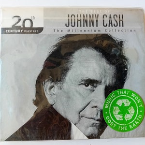 Peut inclure: Une photo en noir et blanc de Johnny Cash sur une pochette de CD. Le titre indique "The Best of Johnny Cash: The Millennium Collection". Le CD fait partie de la série 20th Century Masters.