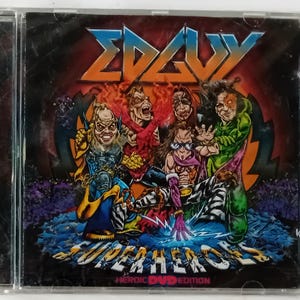 Op de afbeelding: CD-hoesje met de bandnaam "ΣΔΑΥ" in oranje en blauw, en een groep cartoonfiguren. De albumtitel "SUPERHEROES" staat eronder, met "HEROIC DVD EDITION" onderaan. De achtergrond is een mix van rood, paars en blauw.
