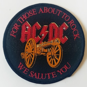 Peut inclure: Un écusson brodé noir et rouge avec le texte "For Those About To Rock We Salute You" et le logo AC/DC avec un canon au centre.