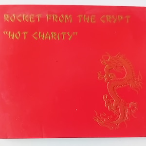Può includere: Un quadrato rosso con testo dorato che recita "ROCKET FROM THE CRYPT" e "HOT CHARITY". Un disegno di drago dorato è sul lato destro del quadrato. Lo sfondo è di colore rosso pieno.