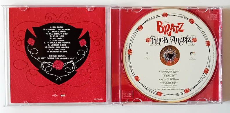 Puede incluir: Un CD de m&uacute;sica Bratz Rock Angelz en una caja de pl&aacute;stico transparente. El lado izquierdo presenta un fondo rojo con un escudo negro que contiene una lista de canciones. El lado derecho muestra el disco CD blanco con el logo de Bratz Rock Angelz.